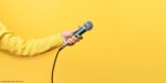 Hand,Holding,Microphone,Over,Yellow,Background,,Panoramic,Mock,Up,Image